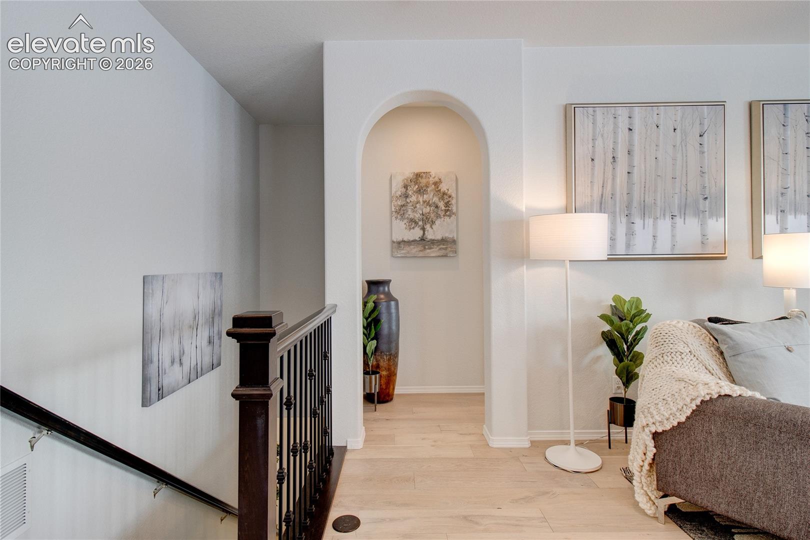 Arched architectural pass-through with wood-finish flooring and staircase featuring a dark wood handrail and metal balusters