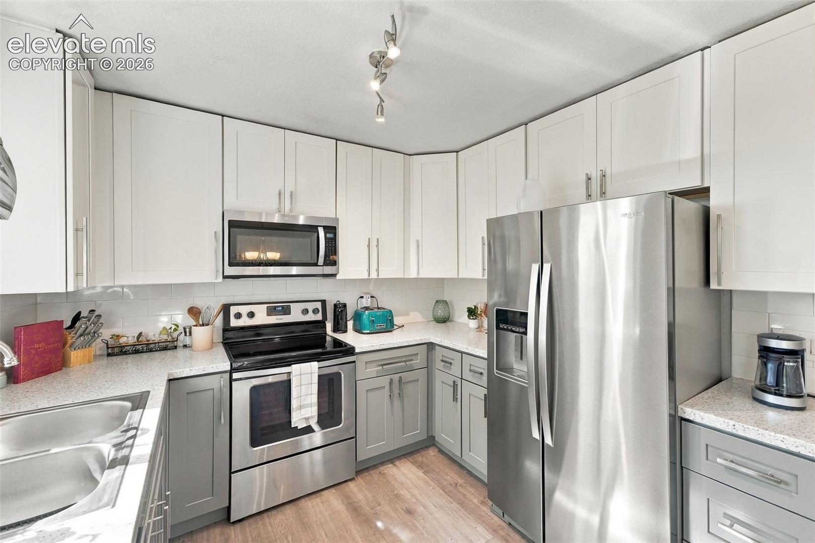 Kitchen with two-tone cabinetry, stainless steel appliances, speckled countertops, white subway tile backsplash, and wood-finish flooring