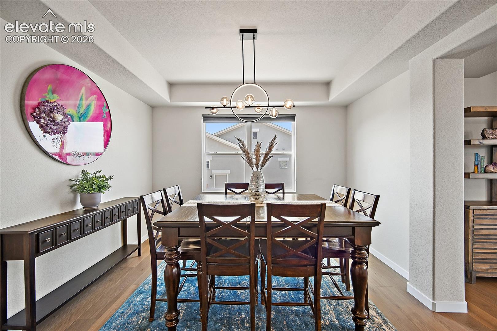 Tray ceiling with a contemporary chandelier, wood-finish flooring, and built-in shelving