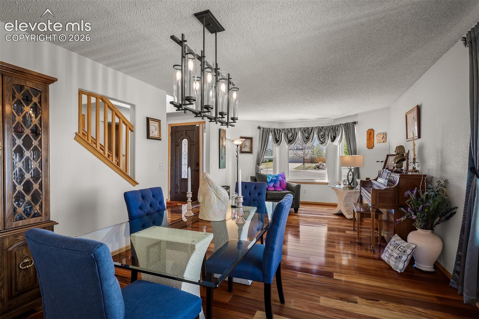 Open-concept dining area featuring Brazilian Koa Hardwood flooring, a modern linear chandelier, and a glass-top dining table.