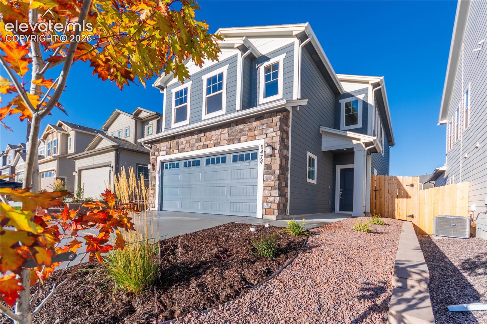 Two-story residence featuring horizontal lap siding, stone veneer accents, an attached two-car garage with transom windows, and a side-yard wood privacy fence