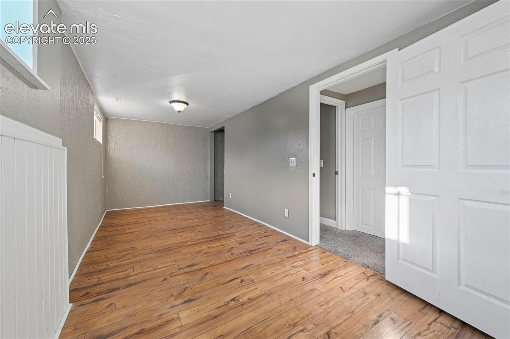 Unstaged bedroom in the basement that is so large/long that it could be an office!    Neutral-toned room featuring LVP flooring, white vertical wainscoting, textured wall surfaces, and two recessed windows (closet in far back) 