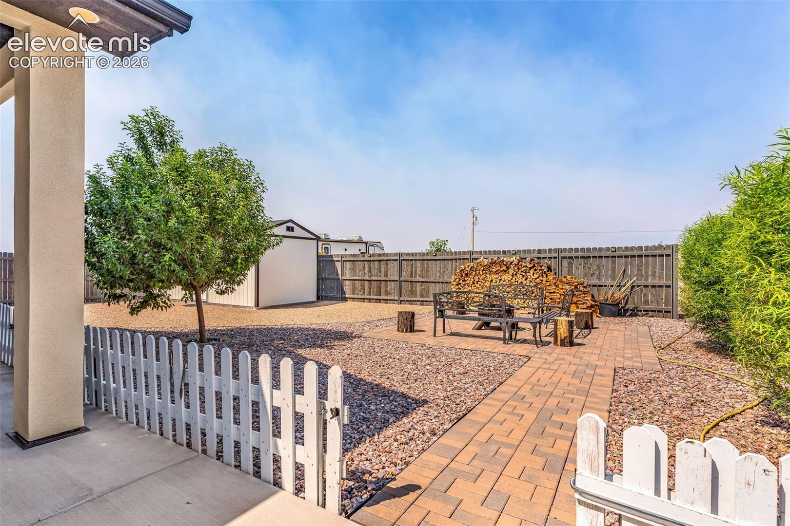 Gravel backyard with a picket fence entry, paver pathway, and a detached storage shed