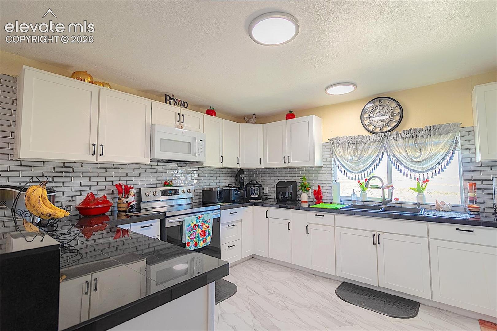 Kitchen featuring white microwave, stainless steel electric range, a sink, dark countertops, and light marble finish floors