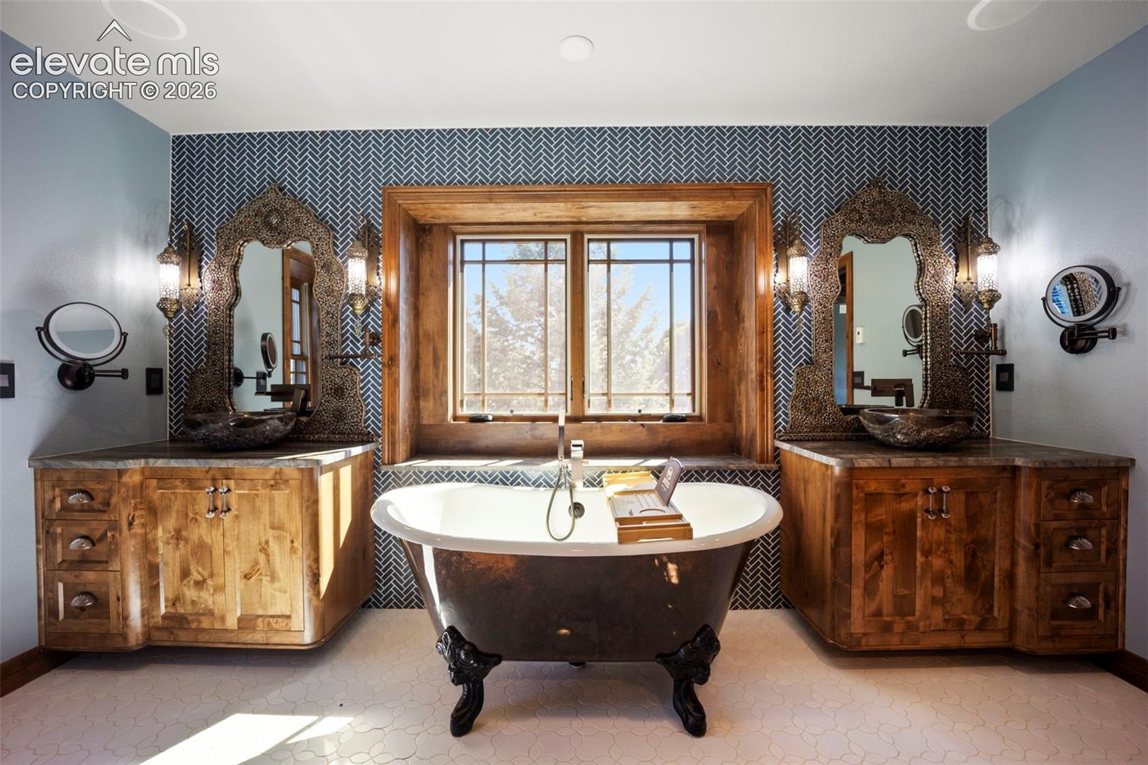 Freestanding bathtub with claw feet, flanked by two rustic wood vanities with vessel sinks