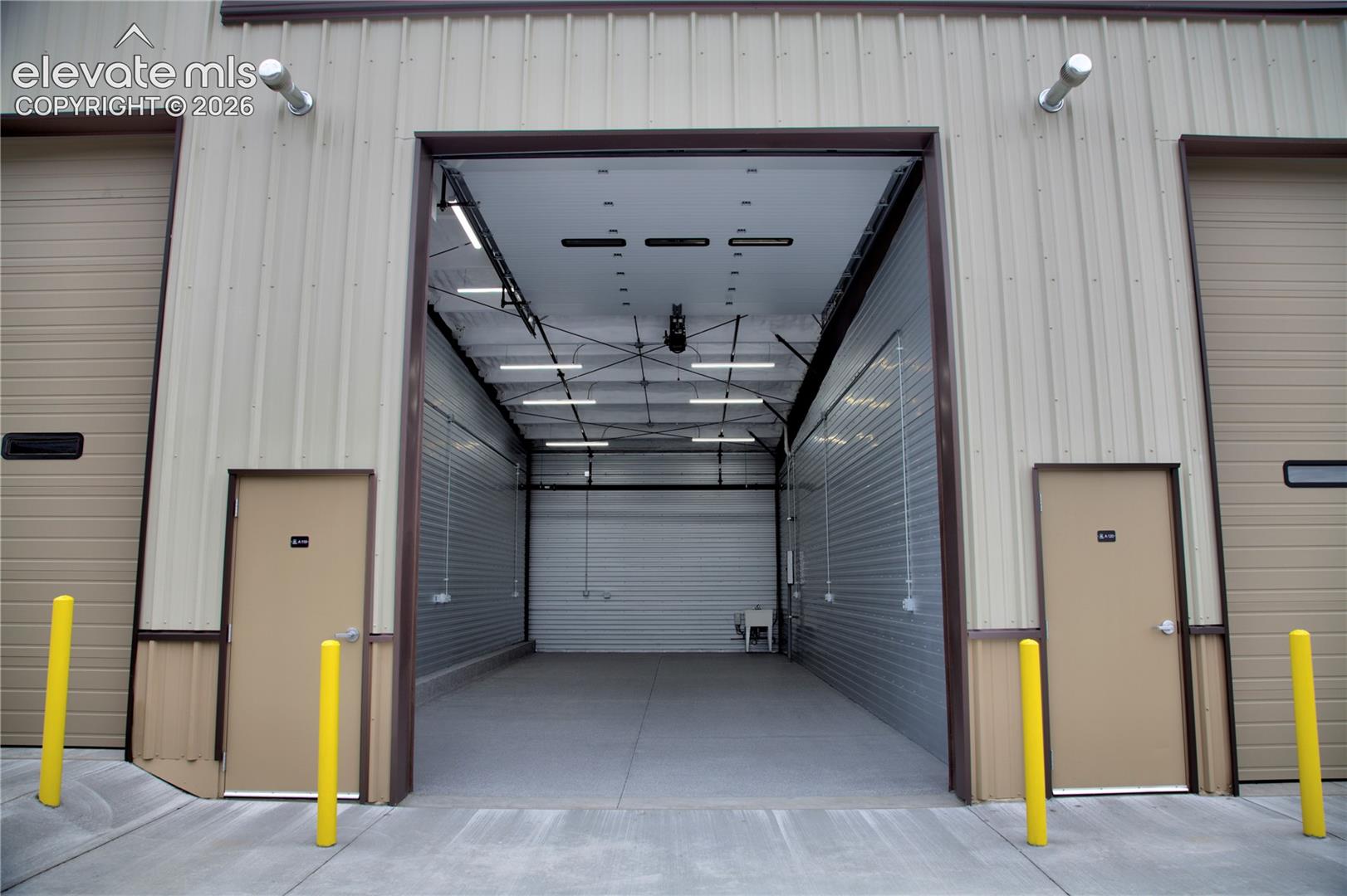 Wide overhead door entrance, concrete flooring, corrugated metal walls, and overhead lighting