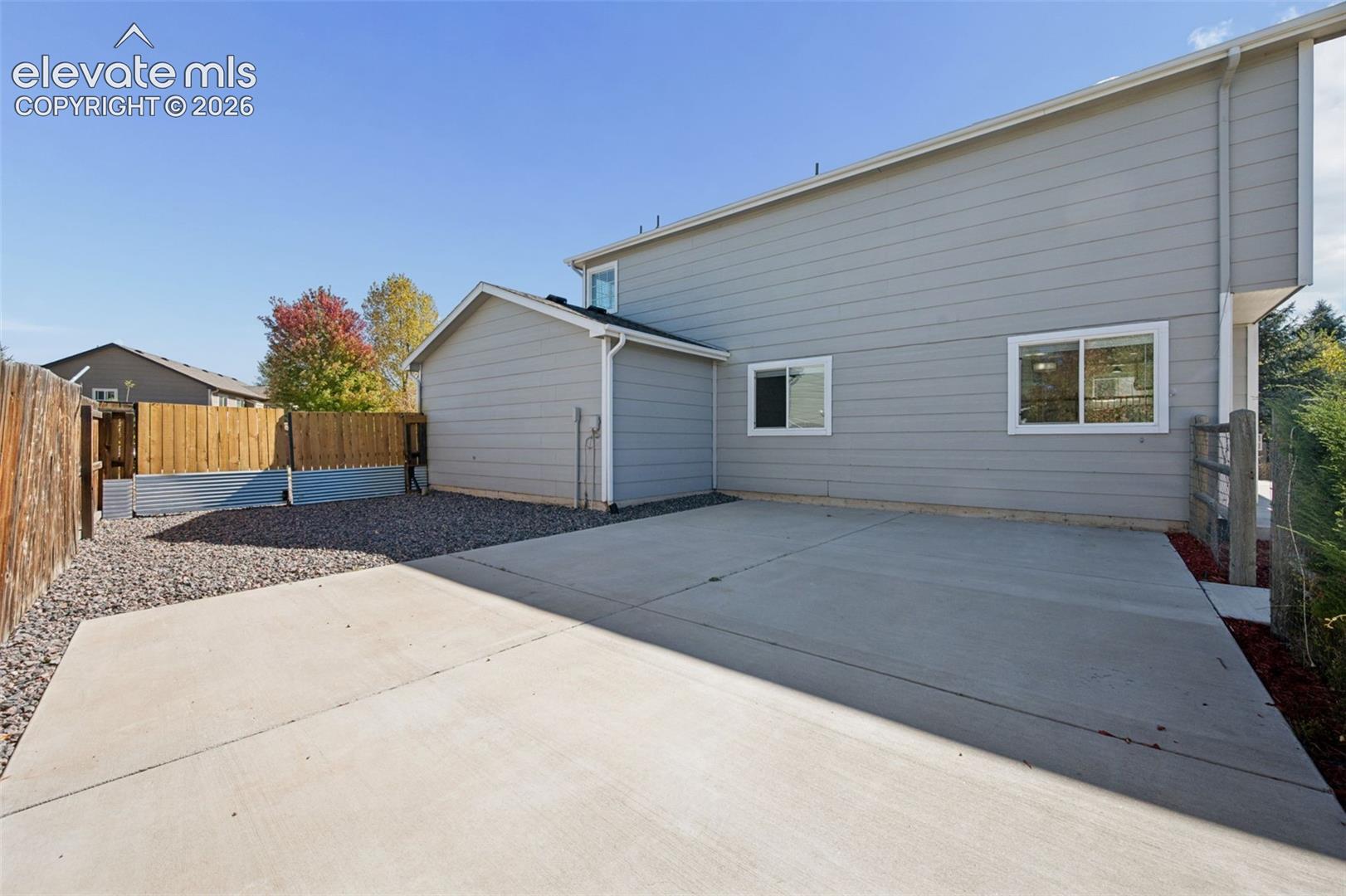 Exterior siding featuring horizontal lap boards, concrete patio, gravel ground cover, and wood perimeter fencing