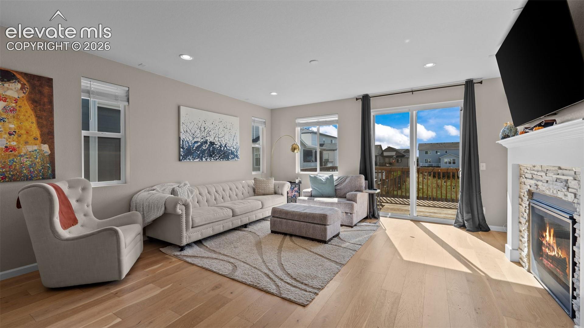Hardwood-finish flooring, recessed lighting, and a fireplace with a stacked stone facade