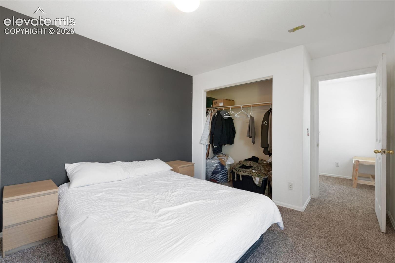 Bedroom featuring a gray accent wall, neutral carpeting, and a built-in closet with a hanging rod