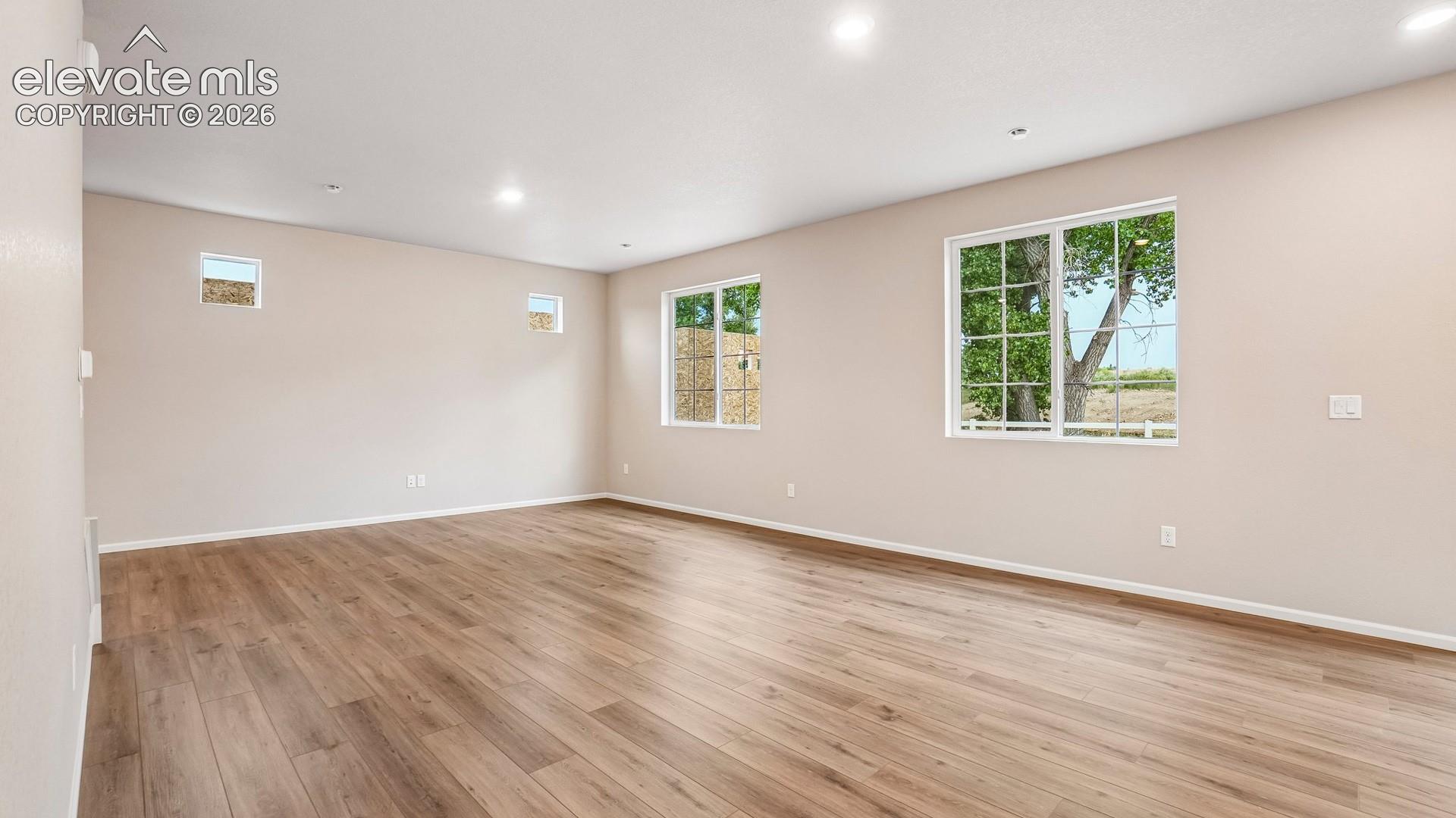 Spacious open room showcasing pristine wood-finish flooring, abundant natural light from multiple large windows, recessed ceiling lighting, and fresh neutral wall finishes
*photos of a model home*