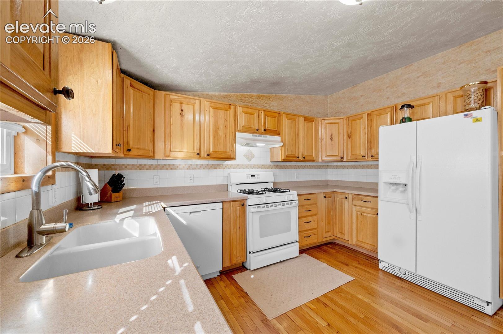 Kitchen with sink, vaulted ceiling, light wood-type flooring, a textured ceiling, and white appliances