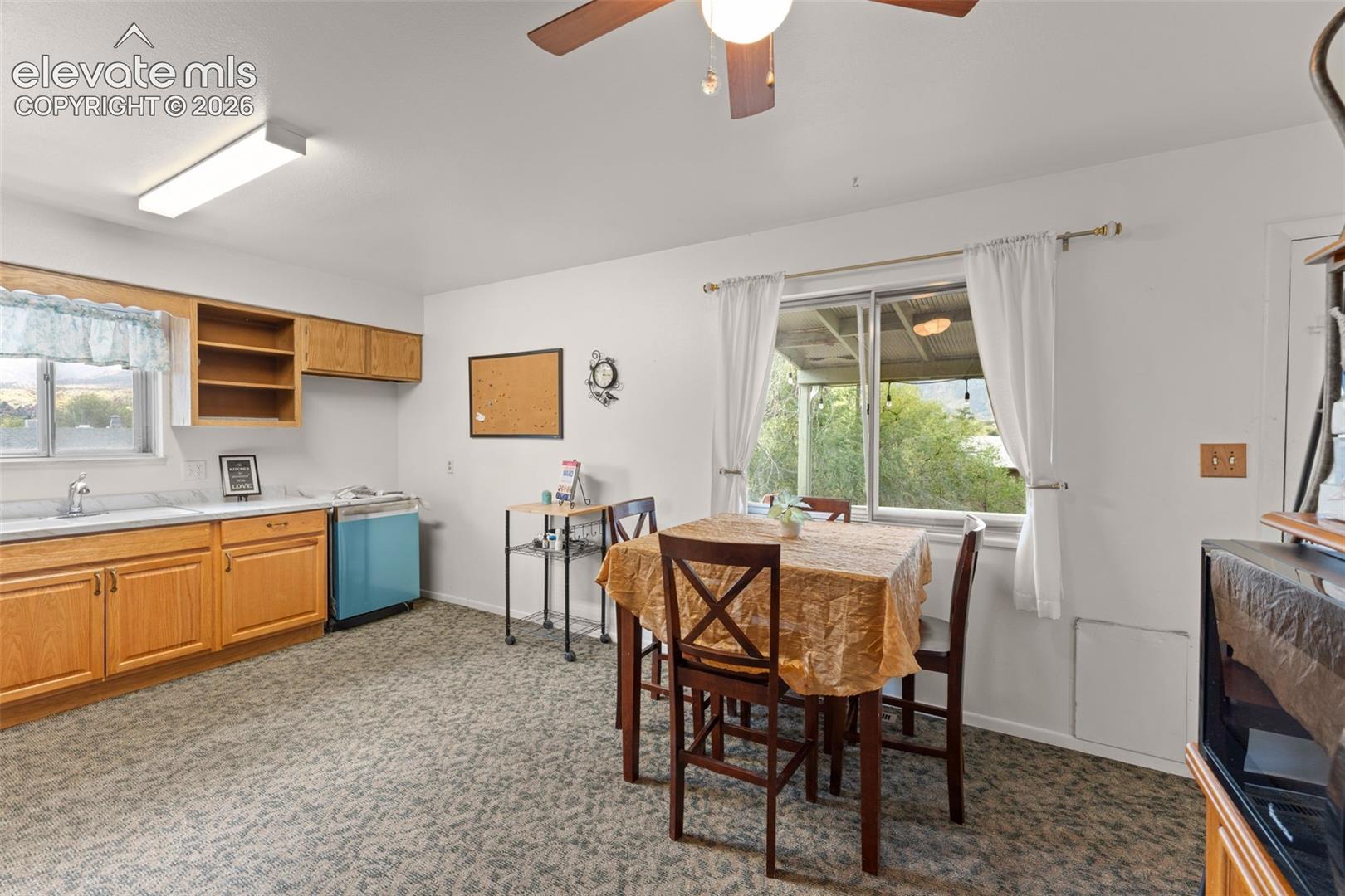Wood-finish cabinetry, built-in shelving, white countertops, ceiling fan with integrated lighting, and a sliding glass window