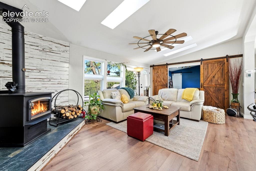 Wood-finish flooring, vaulted ceiling with skylights, wood-burning stove with stone hearth, distressed wood accent wall, and double barn doors