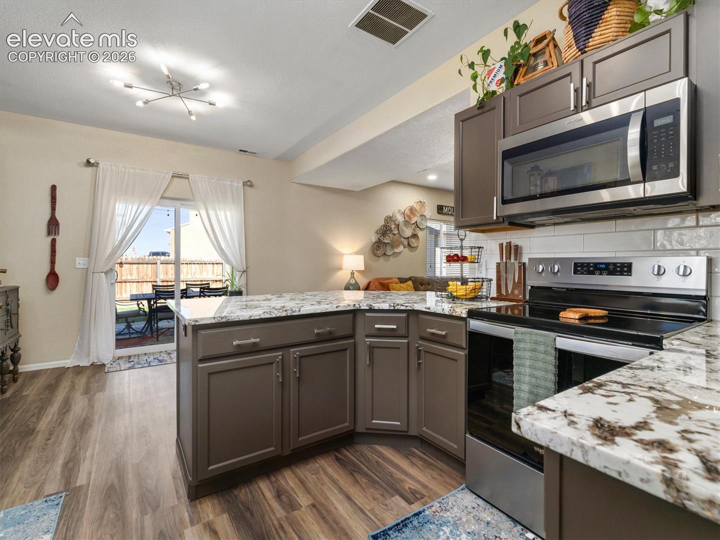 Kitchen featuring LVP flooring, an island with stone-finish countertops, stainless steel appliances, and a sliding glass door