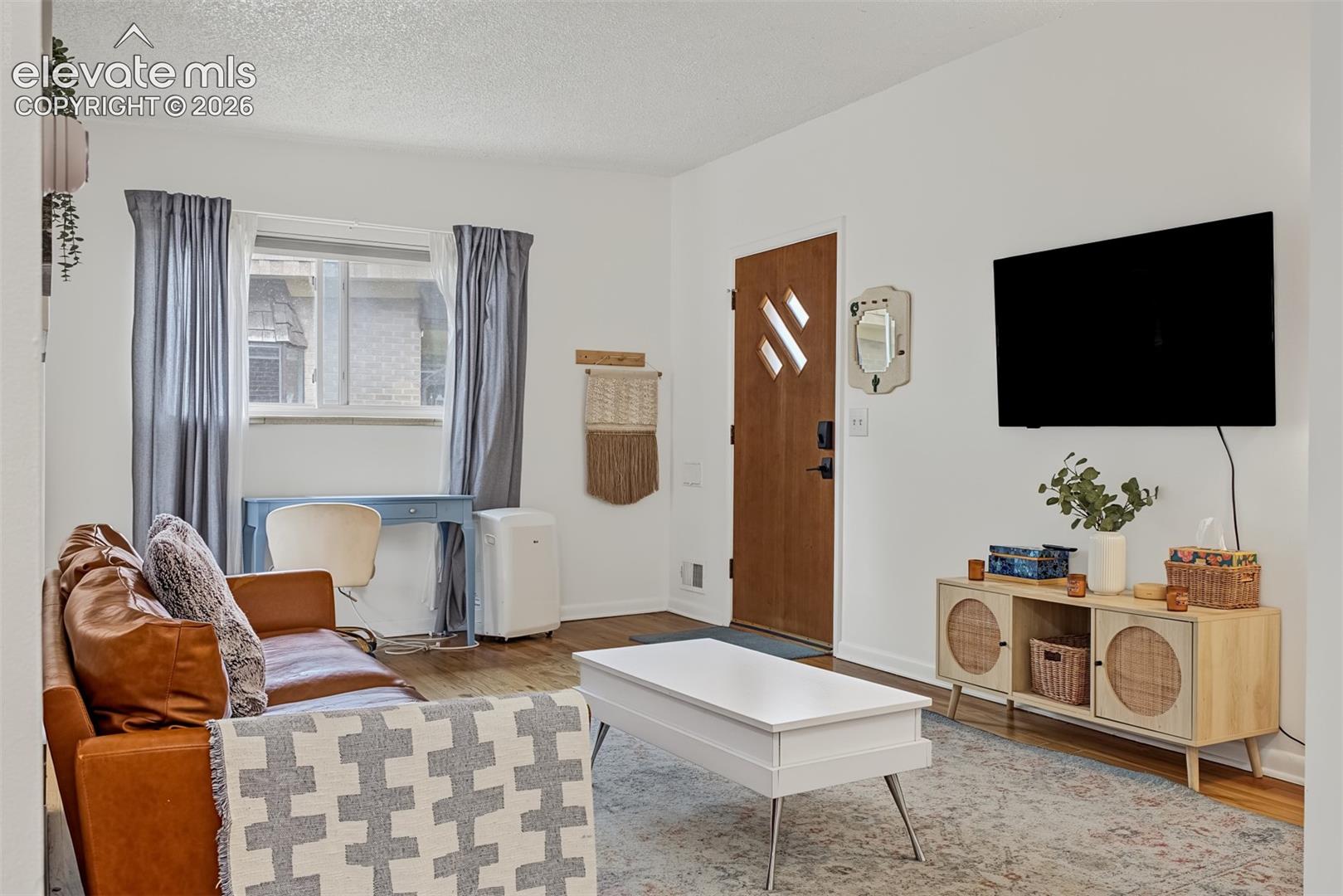 Wood-finish flooring, natural light via a double-pane window, and a solid wood-tone door featuring three rectangular glass insets