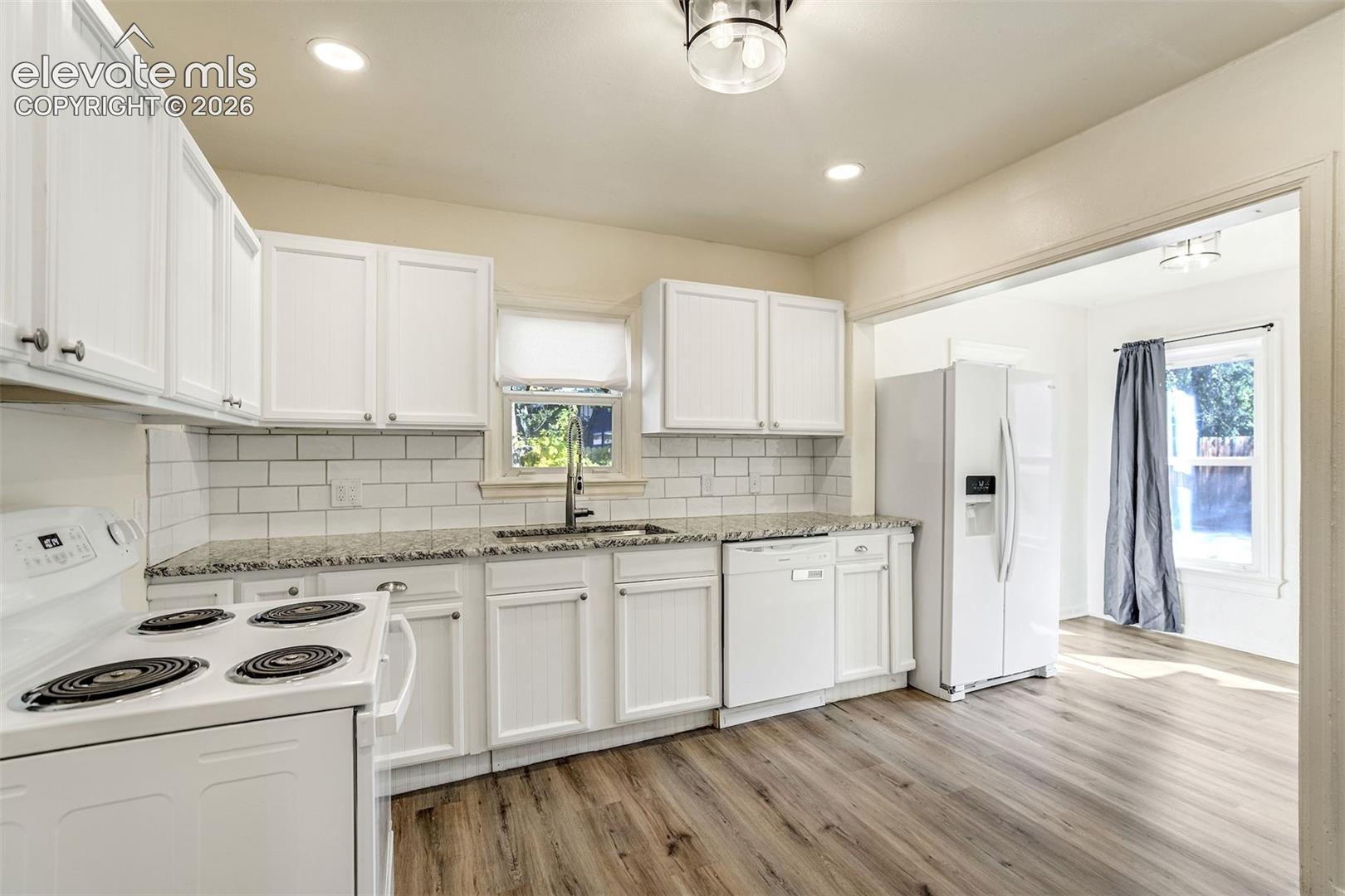 Kitchen featuring white cabinetry, stone-surface countertops, subway tile backsplash, wood-finish flooring, and recessed lighting