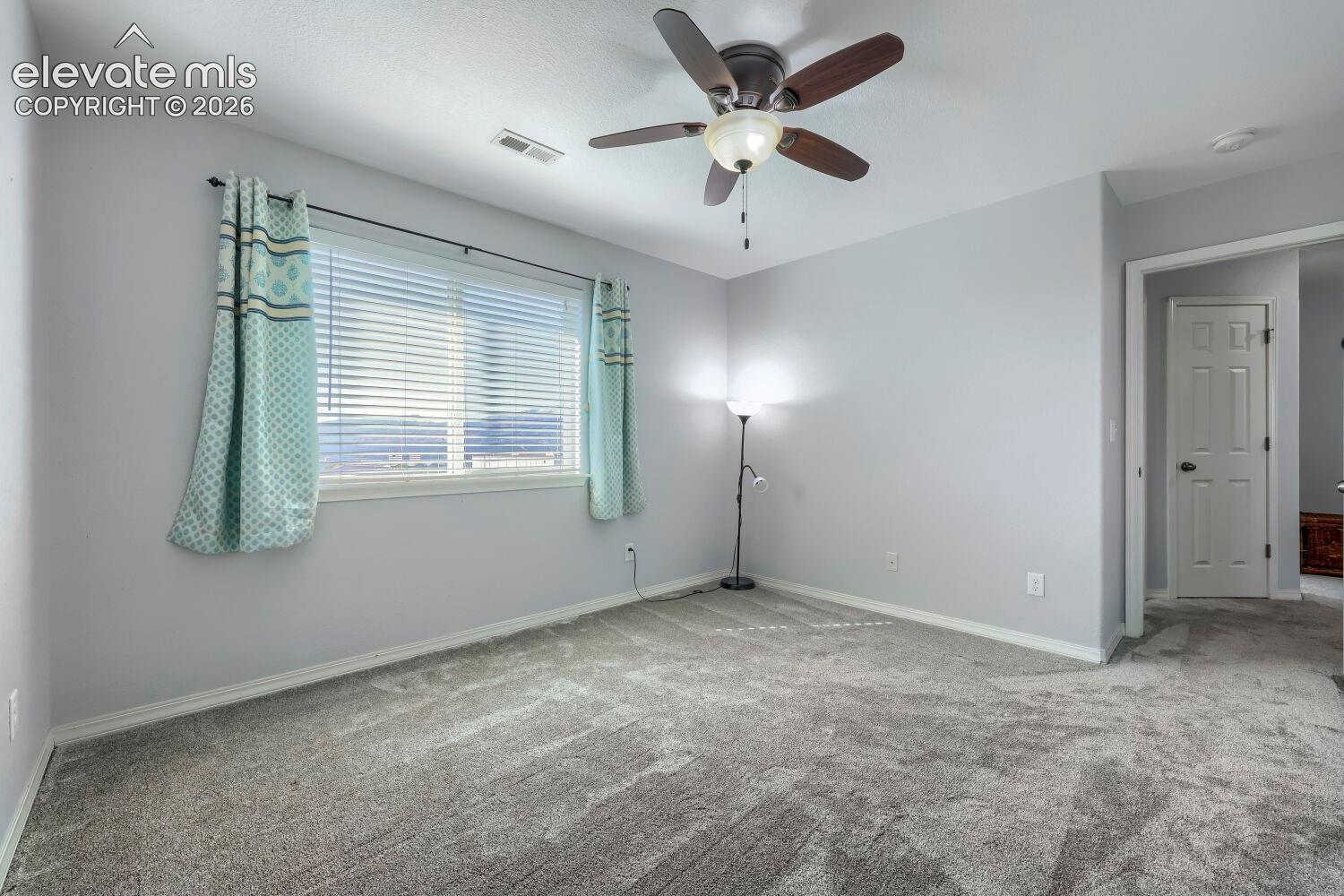 Neutral-toned interior room featuring wall-to-wall carpeting, a multi-blade ceiling fan with integrated lighting, and a single-hung window with horizontal blinds