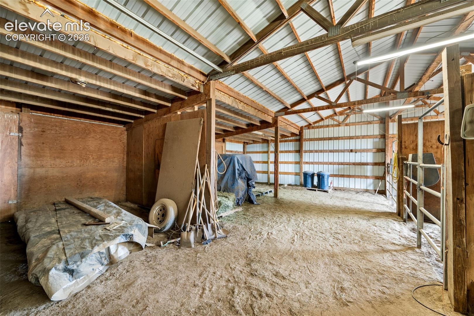 Spacious barn interior featuring exposed wood beams, a corrugated metal roof, and a dirt floor