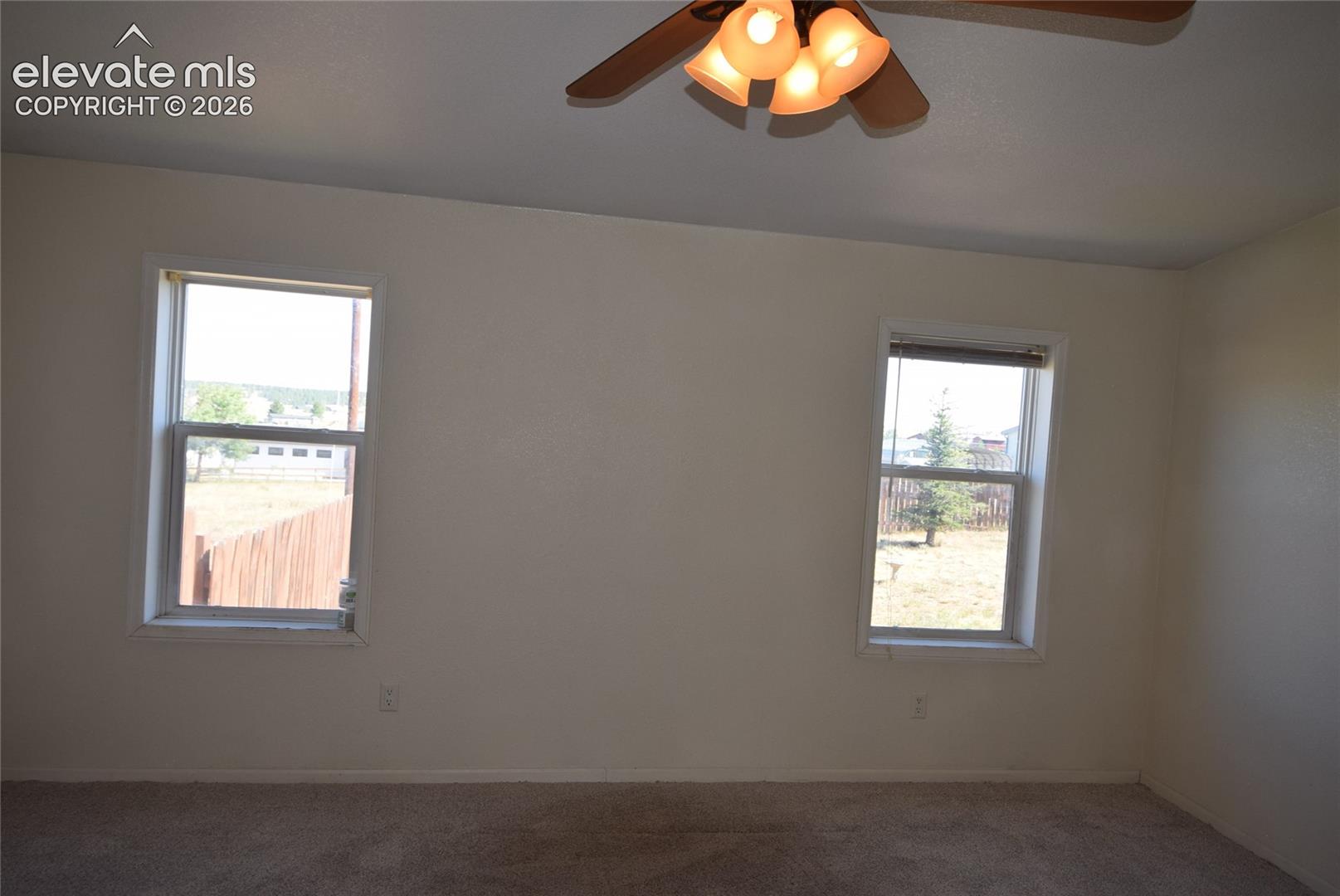 Carpeted flooring with white wall finishes, two windows, and a ceiling fan with integrated lighting