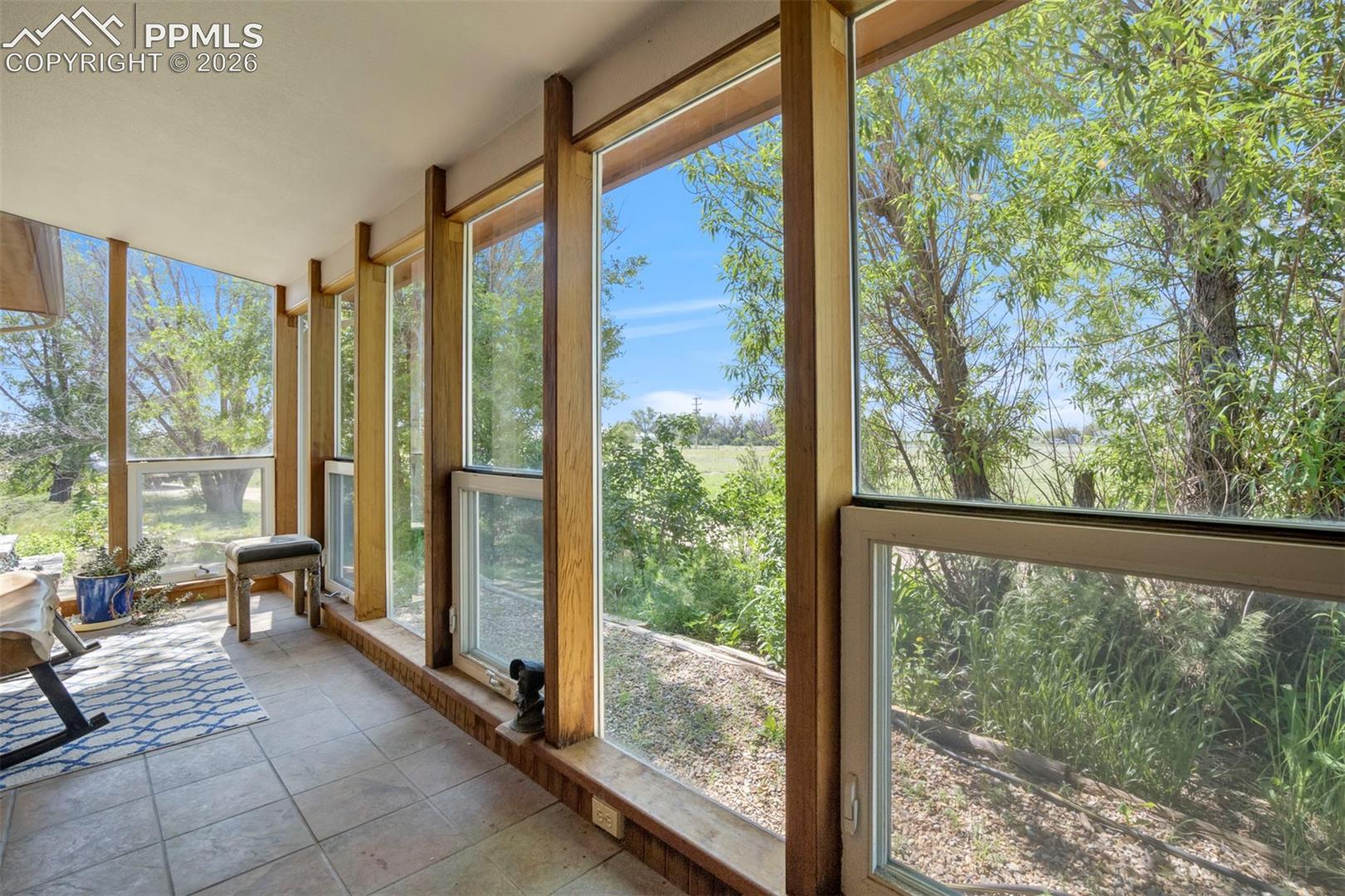 Sunroom featuring extensive window-lined walls, natural wood-finish framing, and tile flooring