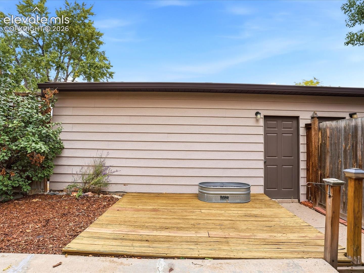 Exterior space featuring a wood deck, horizontal siding, and a solid-panel door with attached wall lighting