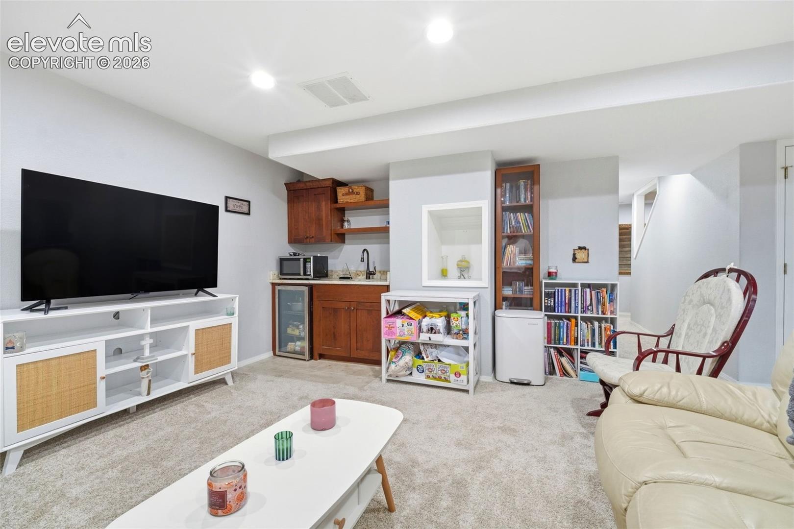 Carpeted lower level featuring a built-in wet bar with wood cabinetry and a beverage refrigerator