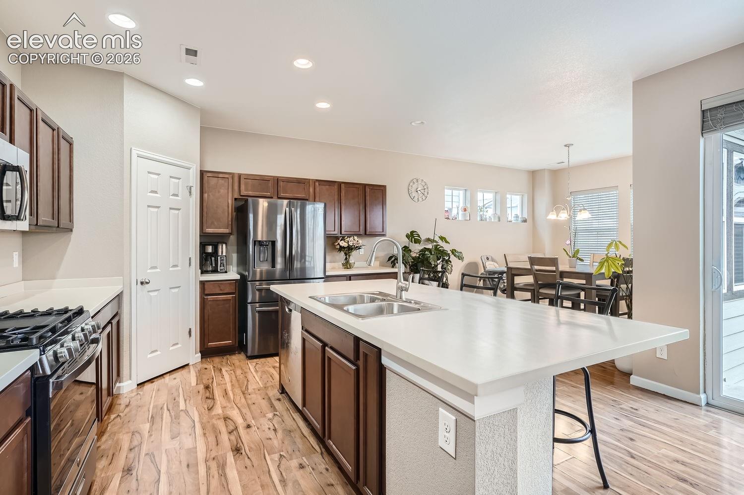 Kitchen featuring wood-finish cabinetry, stainless steel appliances, a central island with a dual-basin sink, and wood-finish flooring