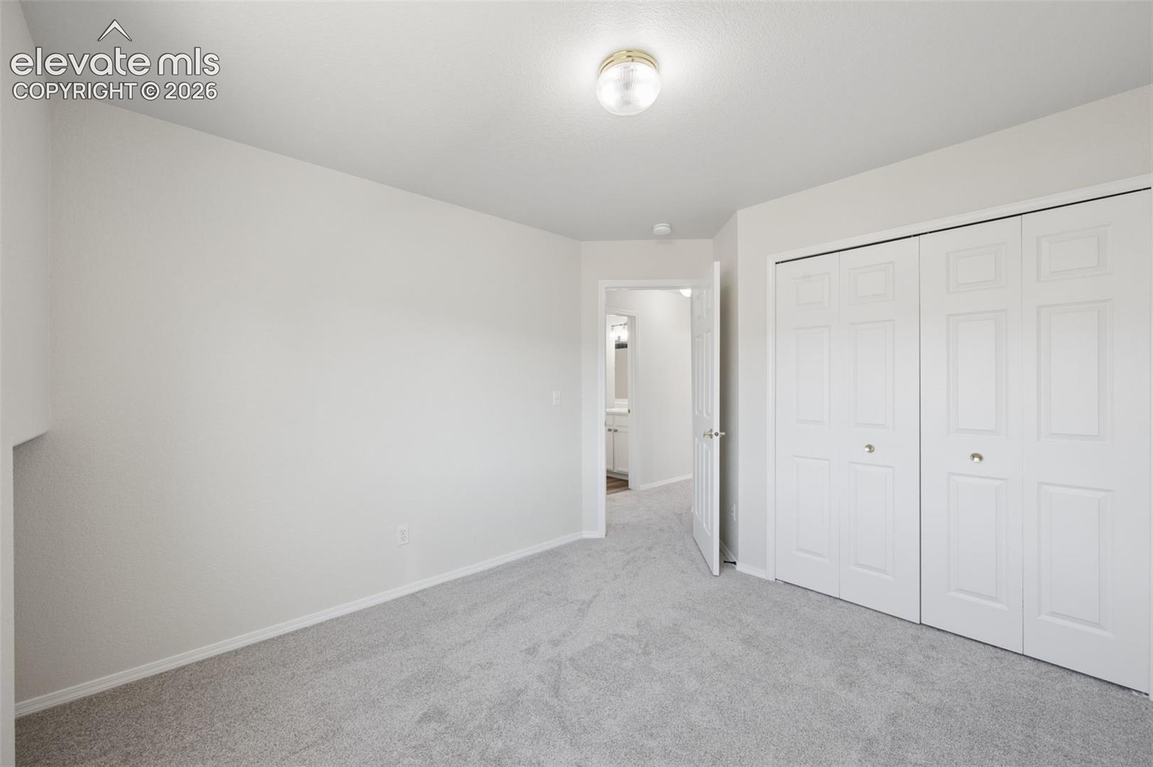 Neutral-toned wall-to-wall carpeting, flush-mount ceiling lighting, and built-in closet with six-panel doors