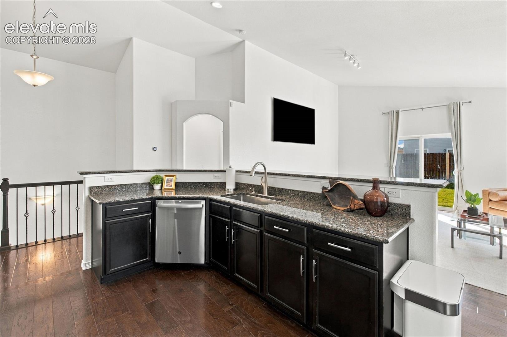 Kitchen featuring dark cabinetry, stone-finish countertops, stainless steel undermount sink, built-in dishwasher, and wood-finish flooring