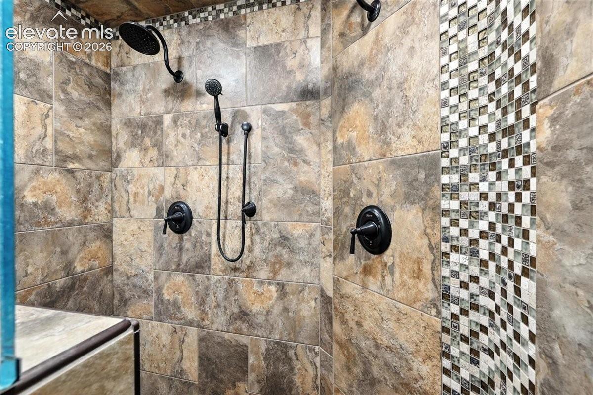 Walk-in shower featuring large-format neutral-toned tile, a vertical mosaic tile accent band, dual matte black shower heads, and an integrated handheld sprayer