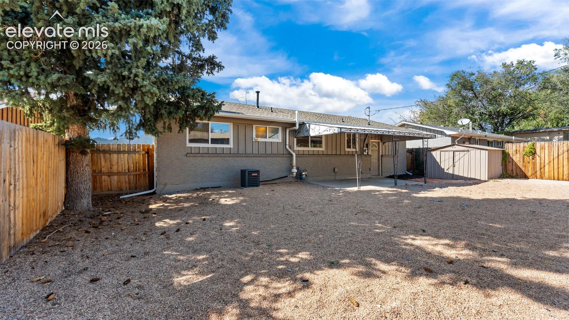 Expansive gravel backyard featuring a covered patio, a storage shed, and wood fencing