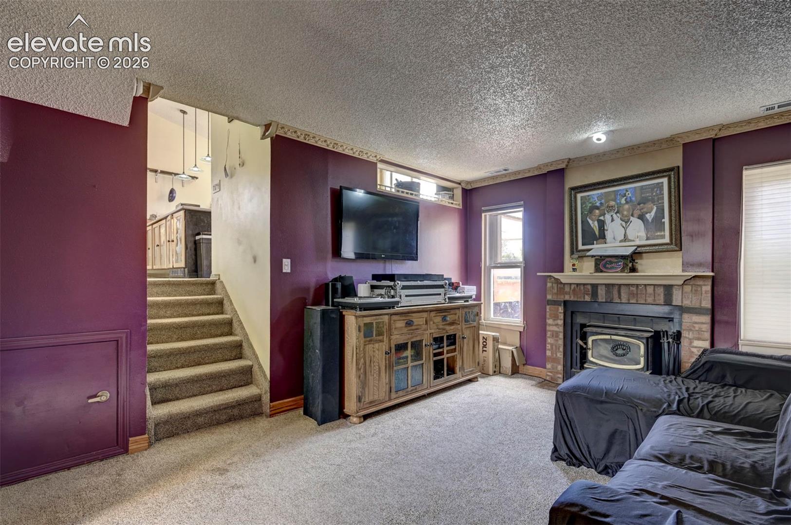 Carpeted living area featuring a brick-surround fireplace with a wood mantle, textured ceiling, and recessed lighting