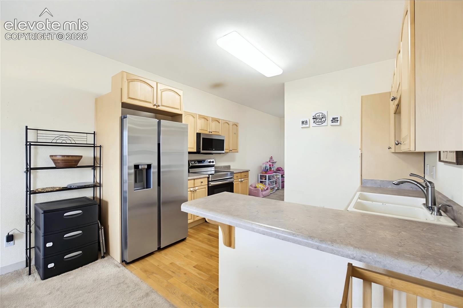Wood-finish flooring, stainless steel side-by-side refrigerator, microwave, electric range, and light wood cabinetry
