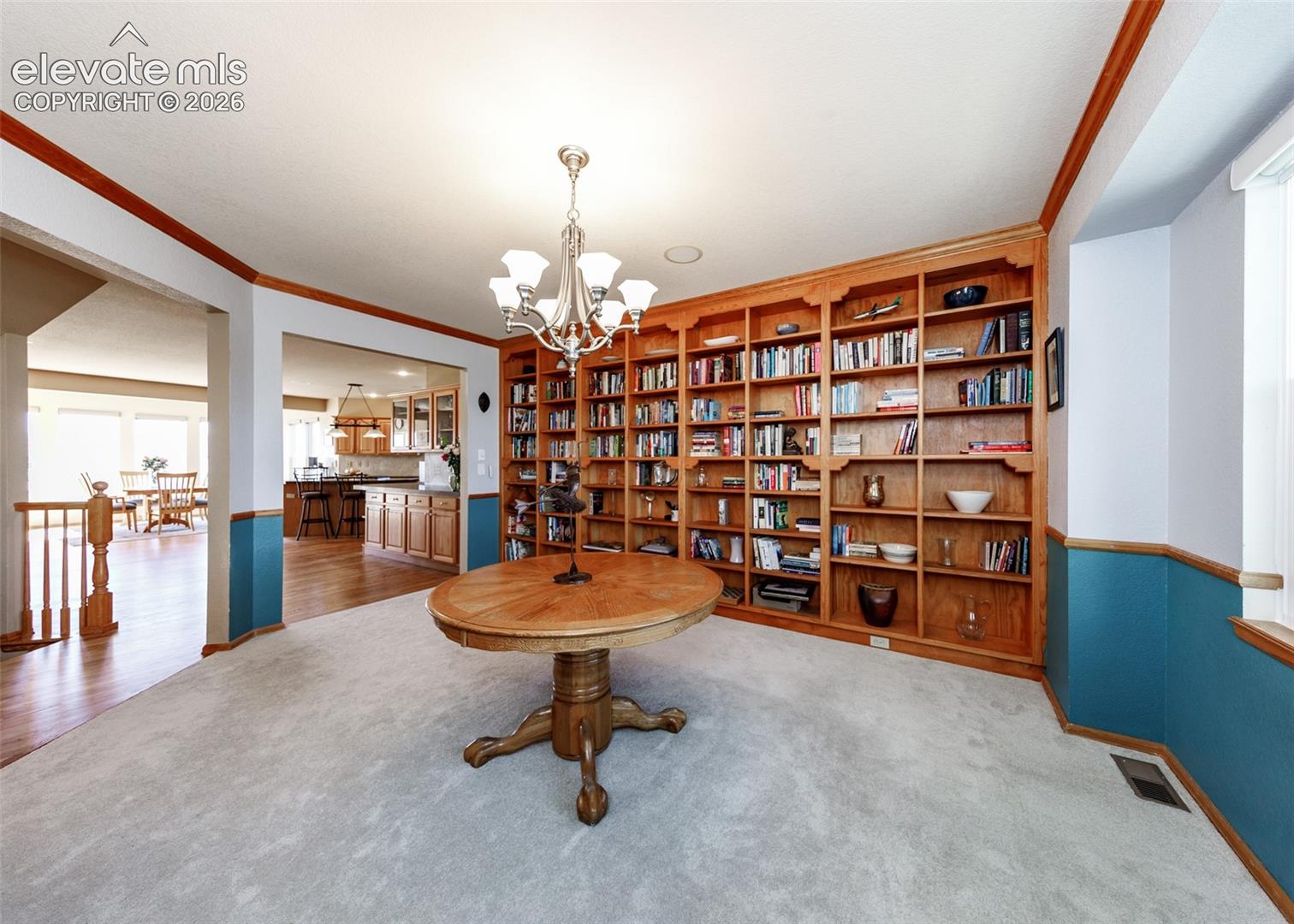 Floor-to-ceiling custom wood shelving, crown molding, chair rail trim, and a multi-arm chandelier fixture