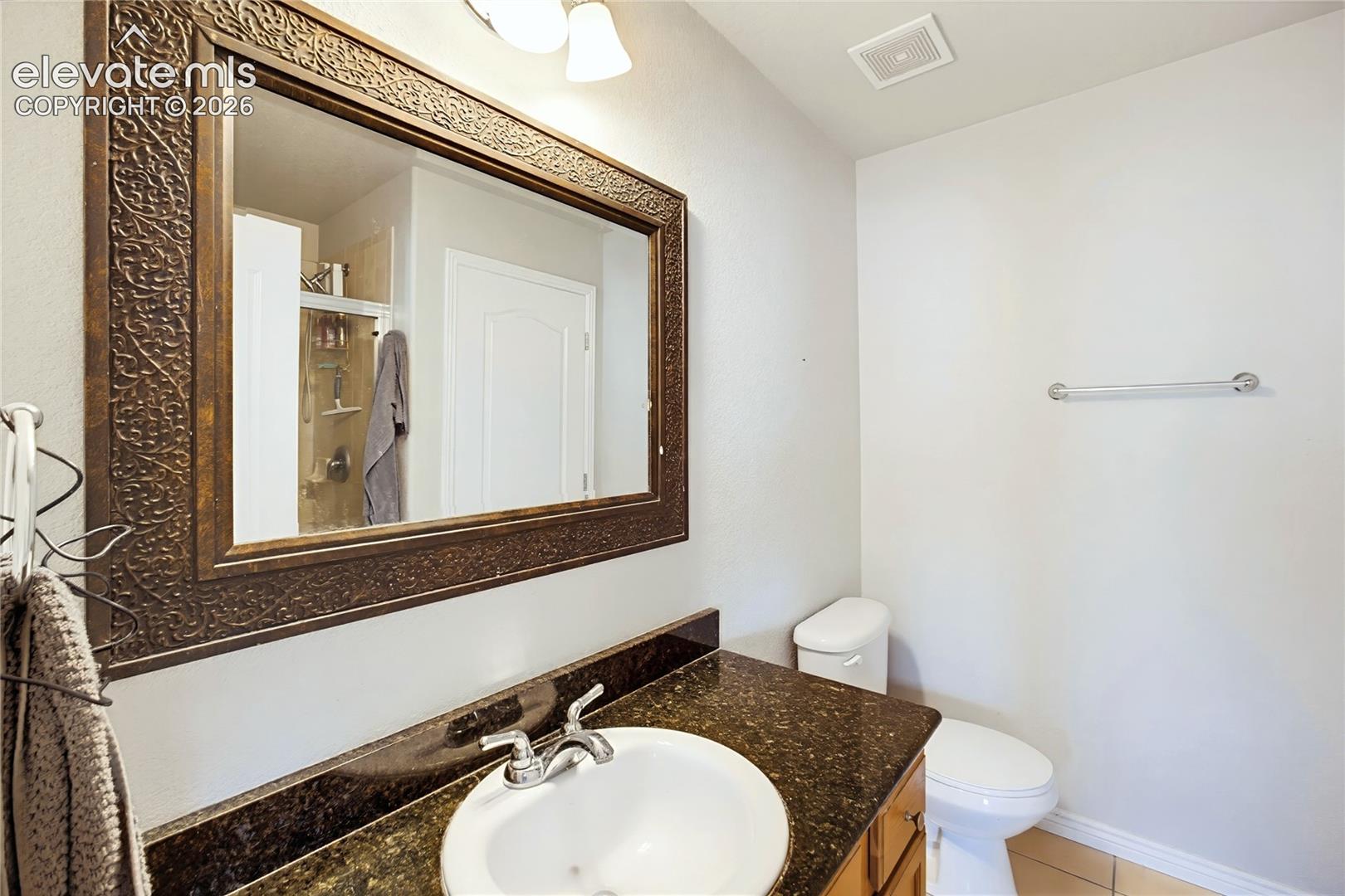 Bathroom featuring a dark stone countertop, integrated oval undermount sink, decorative framed wall mirror, polished chrome faucet, and tile flooring