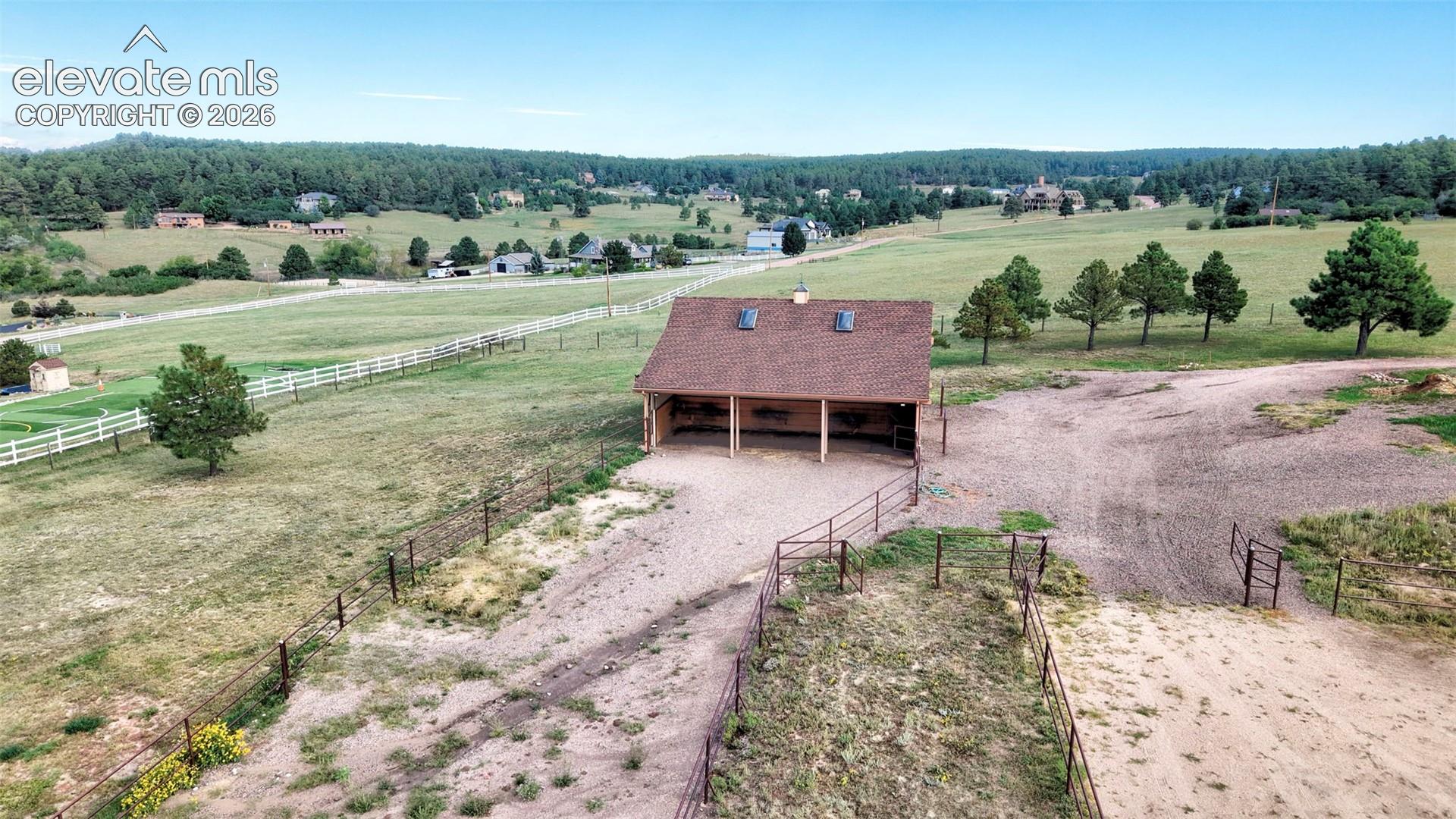 Expansive equestrian facility featuring barn with multiple stalls, fenced paddocks, and a gravel riding area