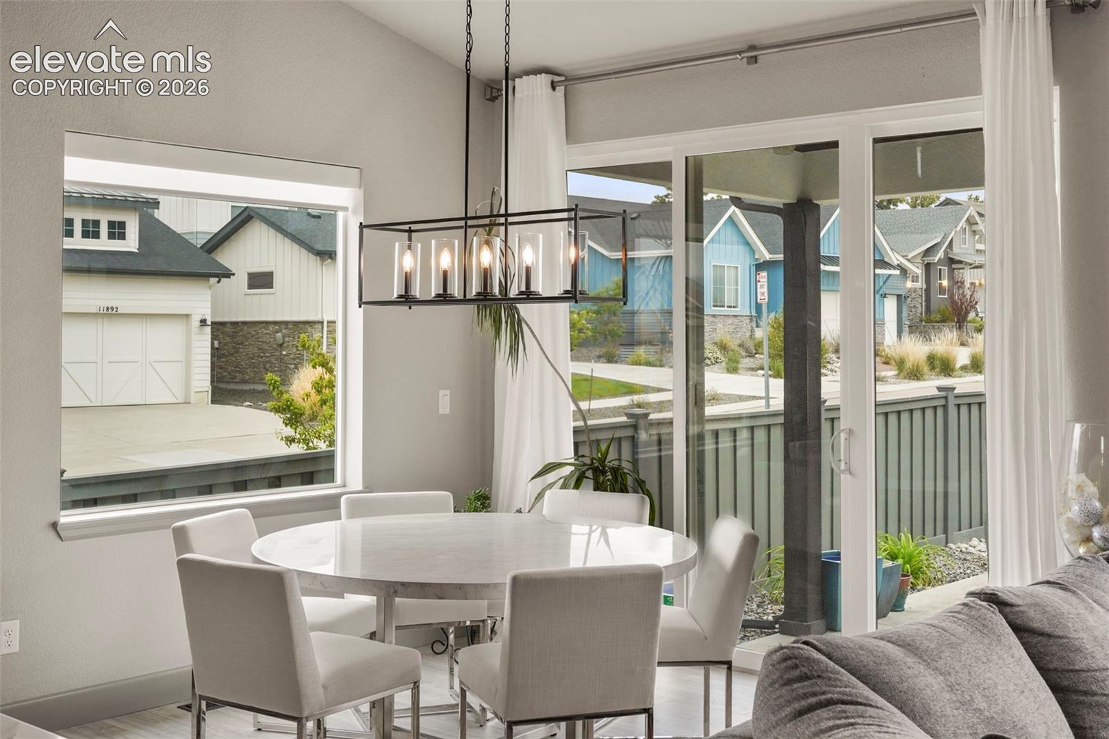 Contemporary dining area featuring a linear chandelier, ample natural light from large windows, and direct access to outdoor space via sliding glass doors