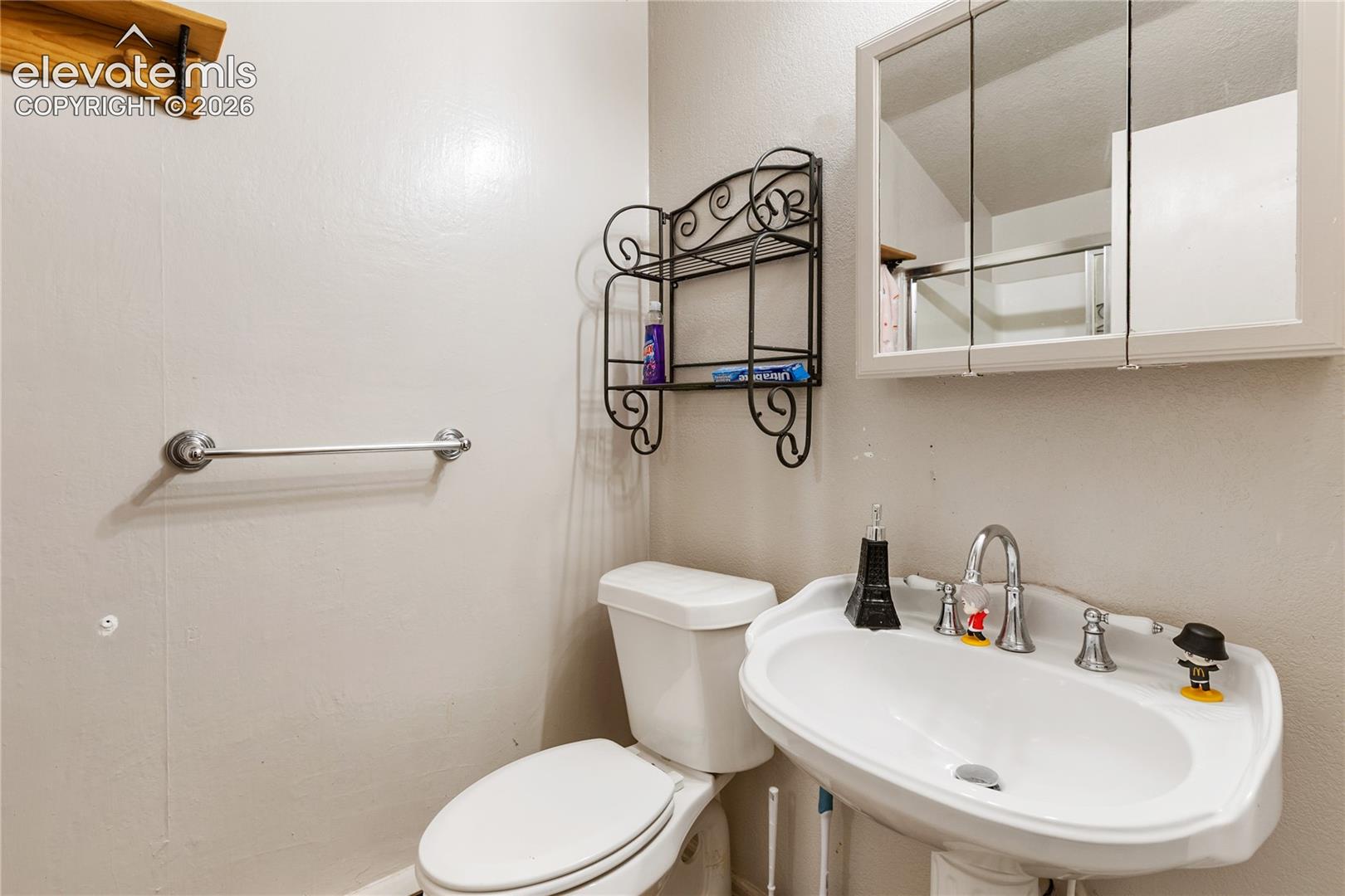 Wall-mounted medicine cabinet with a mirror, pedestal sink with a chrome finish faucet, and an integrated towel bar