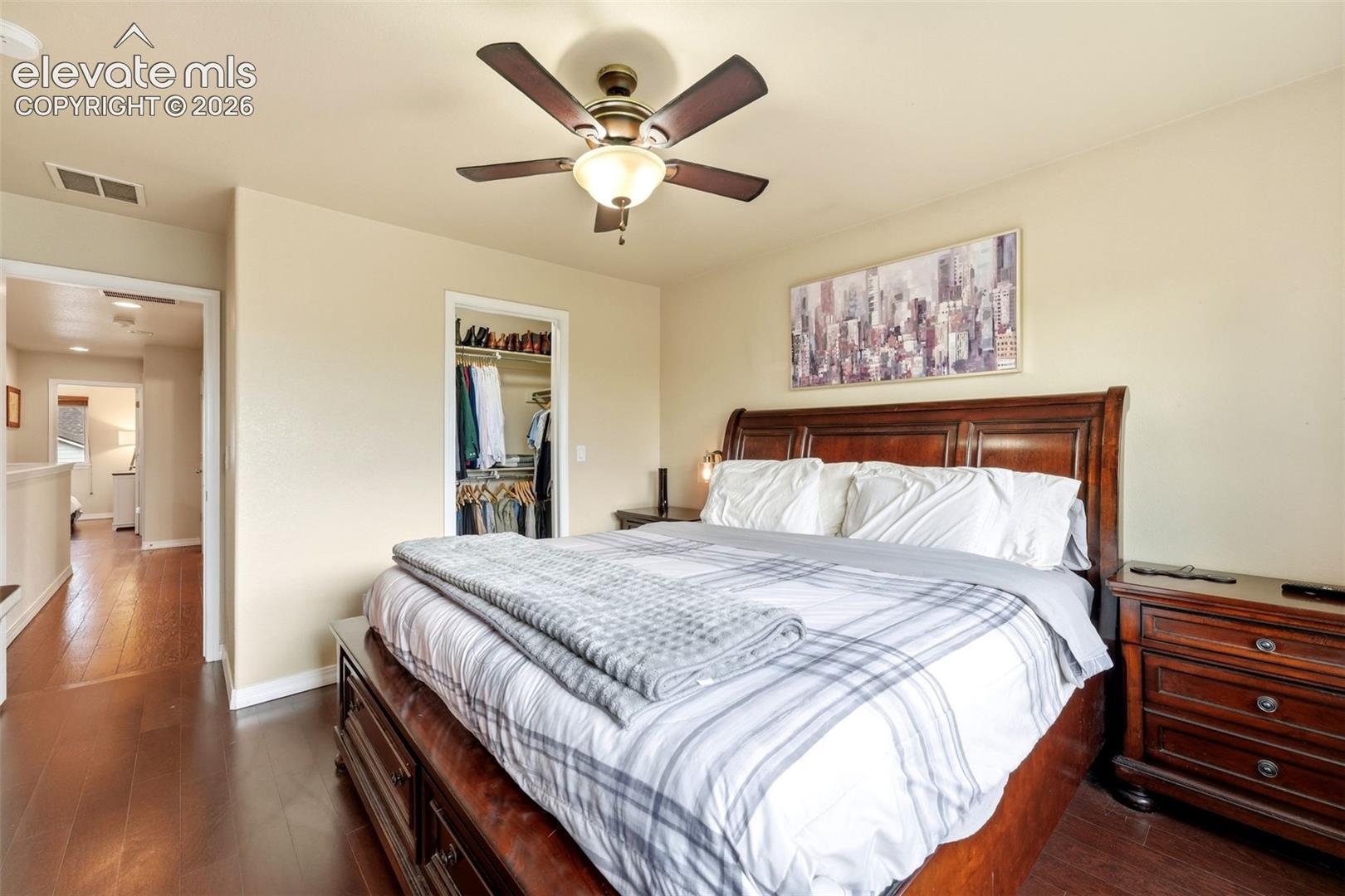 Wood-finish flooring with a ceiling fan light fixture and an open closet with built-in shelving