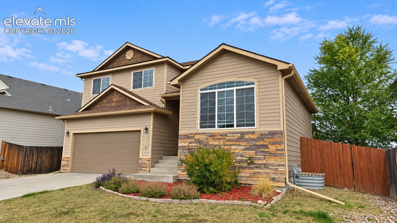 Two-story exterior featuring tan horizontal siding, stone veneer accents, shake-shingle gables, and an attached two-car garage