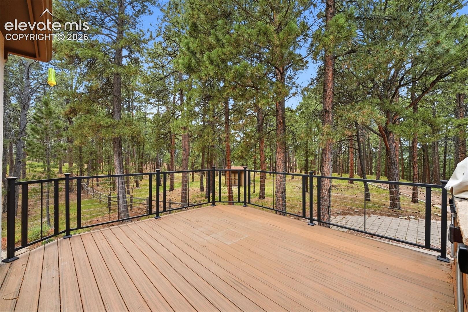 Expansive outdoor deck featuring wood-finish flooring and a black metal railing with glass panels
