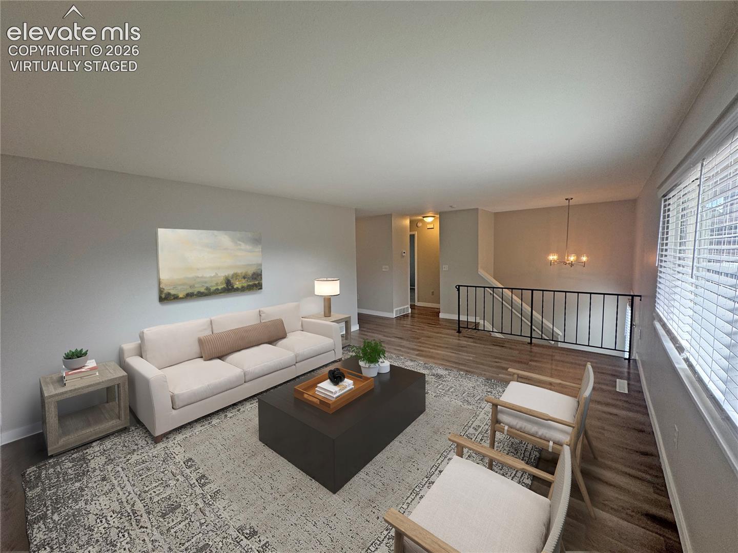 virtually staged Spacious living area featuring wood-finish flooring, a multi-light chandelier, and a metal stair railing