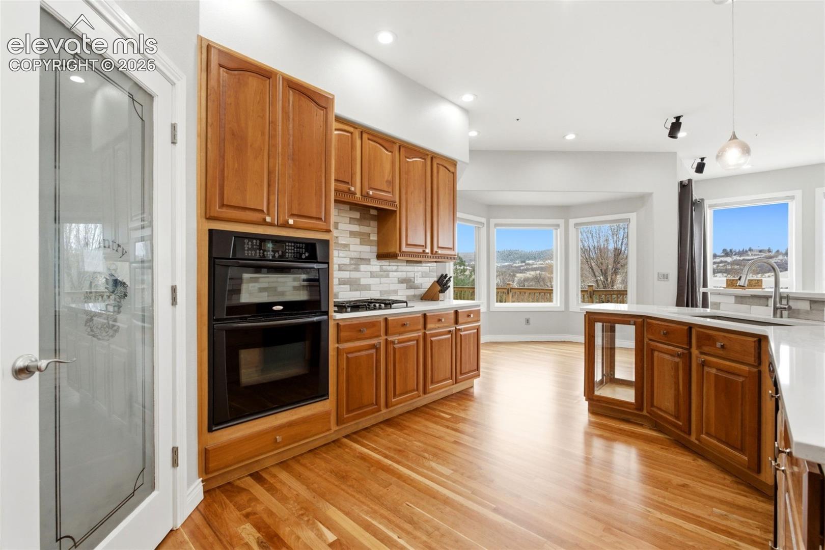 Hardwood flooring, wood cabinetry, built-in double oven, paneled pantry door, and bay windows