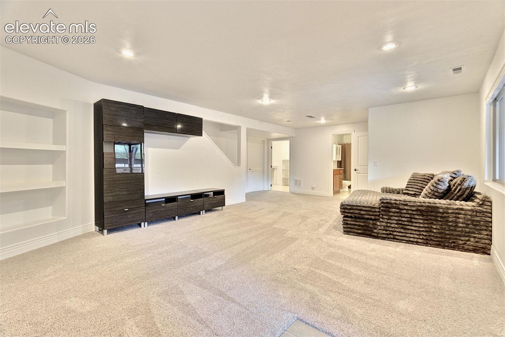 Open interior space featuring recessed ceiling lighting, wall-to-wall carpeting, recessed shelving, and dark wood-finish built-in cabinetry