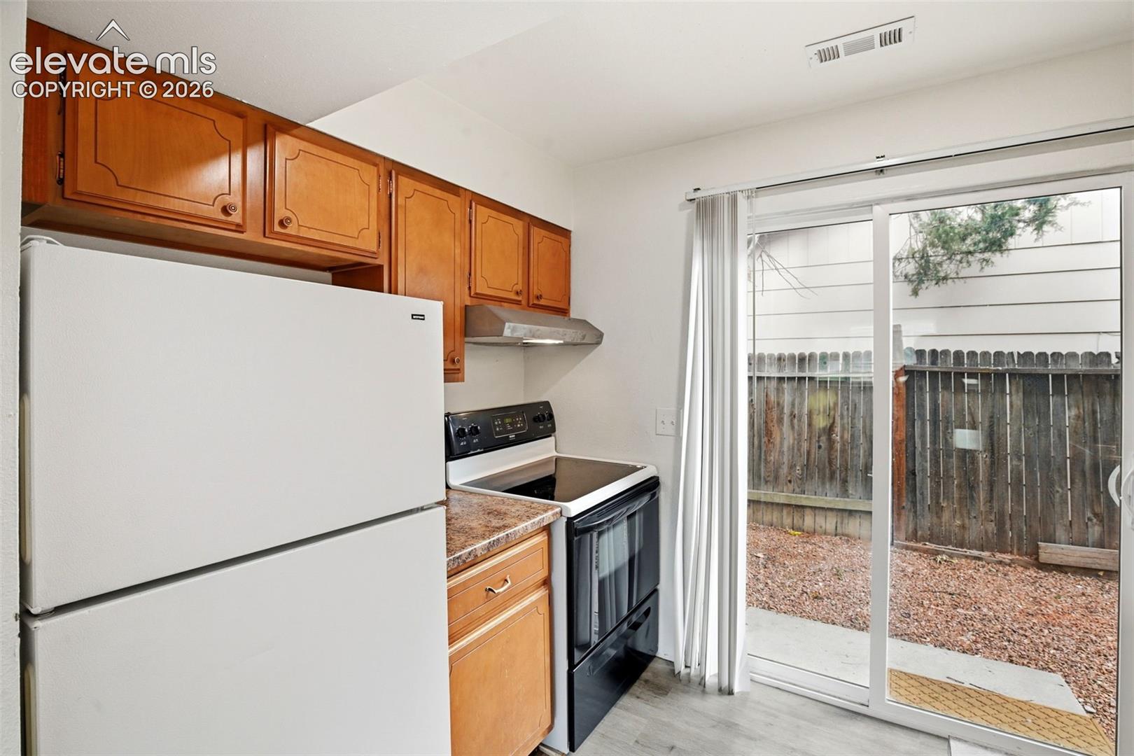 Kitchen with wood-finish cabinetry, white refrigerator, black range, and stone-look countertop