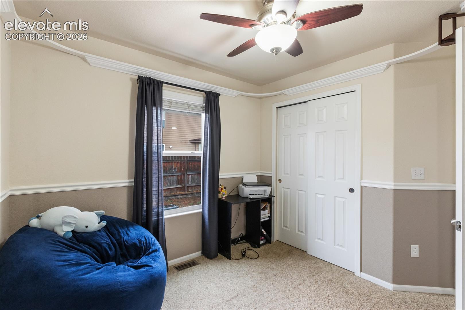 Room featuring crown molding, chair rail trim, carpeted flooring, a ceiling fan with integrated light fixture, and a sliding door closet