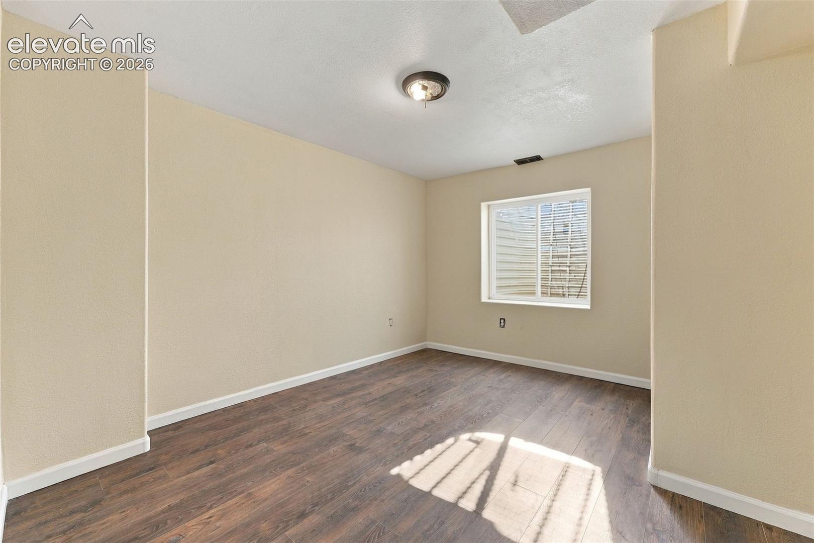 Interior space featuring wood-finish flooring, neutral wall tones, a single-pane sliding window with an egress well, and a flush-mount ceiling light fixture