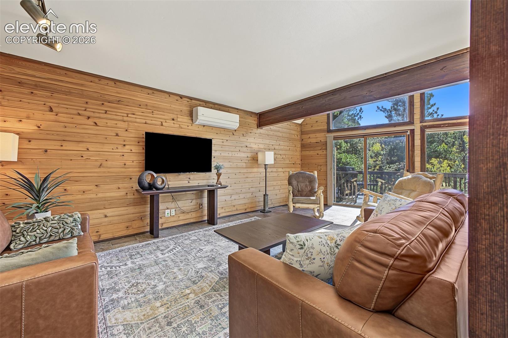 Wood-paneled wall with built-in console, exposed wood beam ceiling, track lighting, and expansive windows