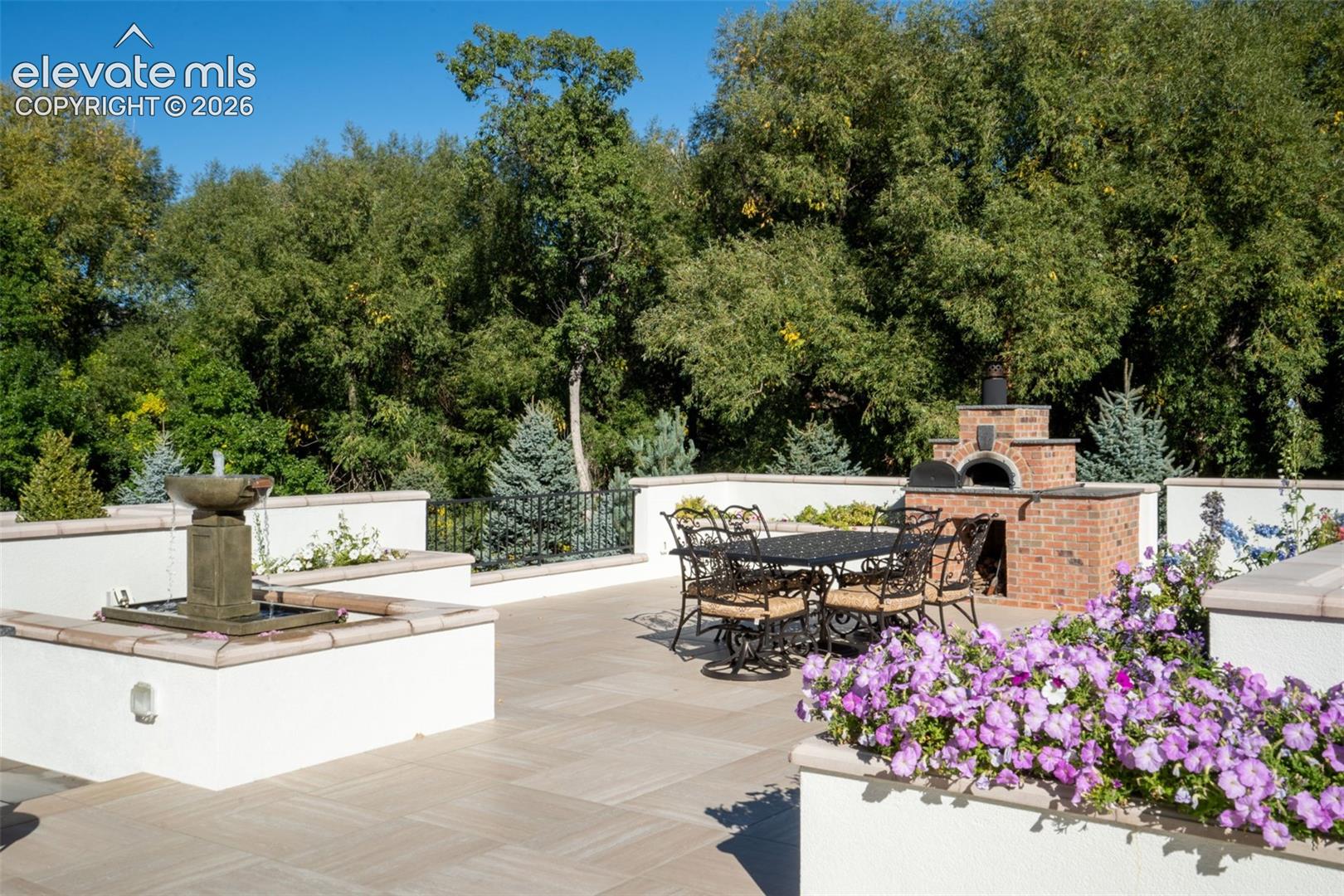 Stone tile terrace featuring a built-in brick oven, decorative stone fountain, raised masonry planters, and wrought iron railing