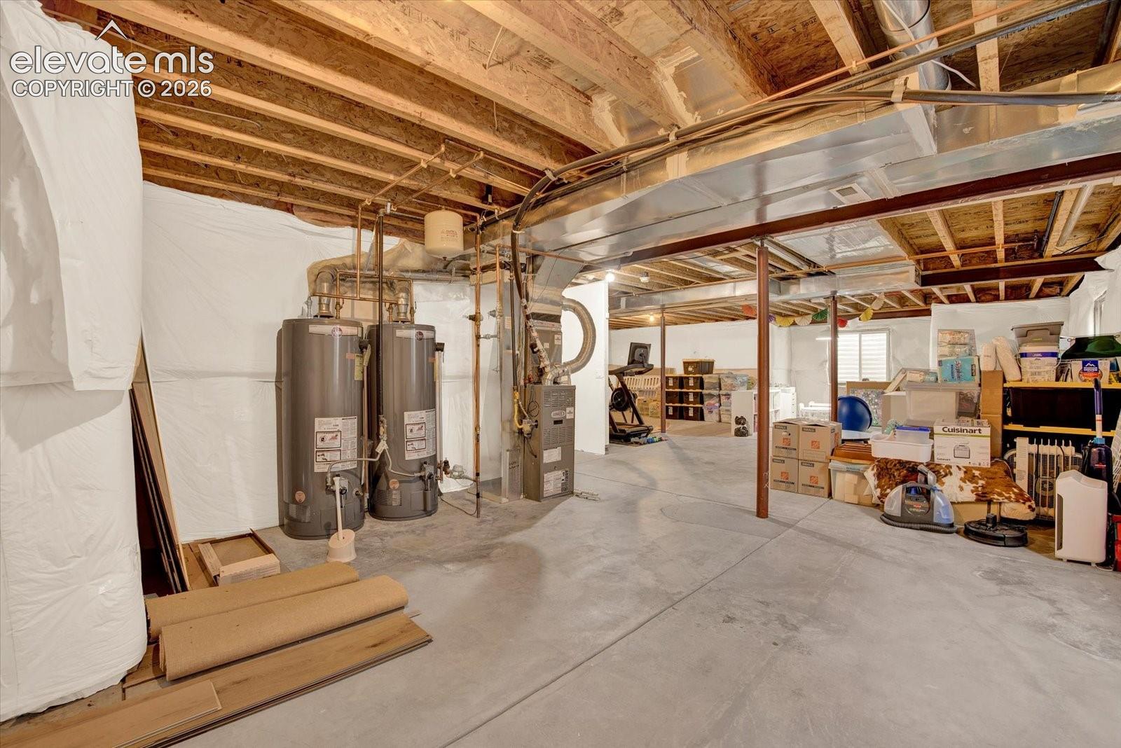 Unfinished basement featuring exposed joists, concrete flooring, dual water heaters, and a central forced-air furnace unit